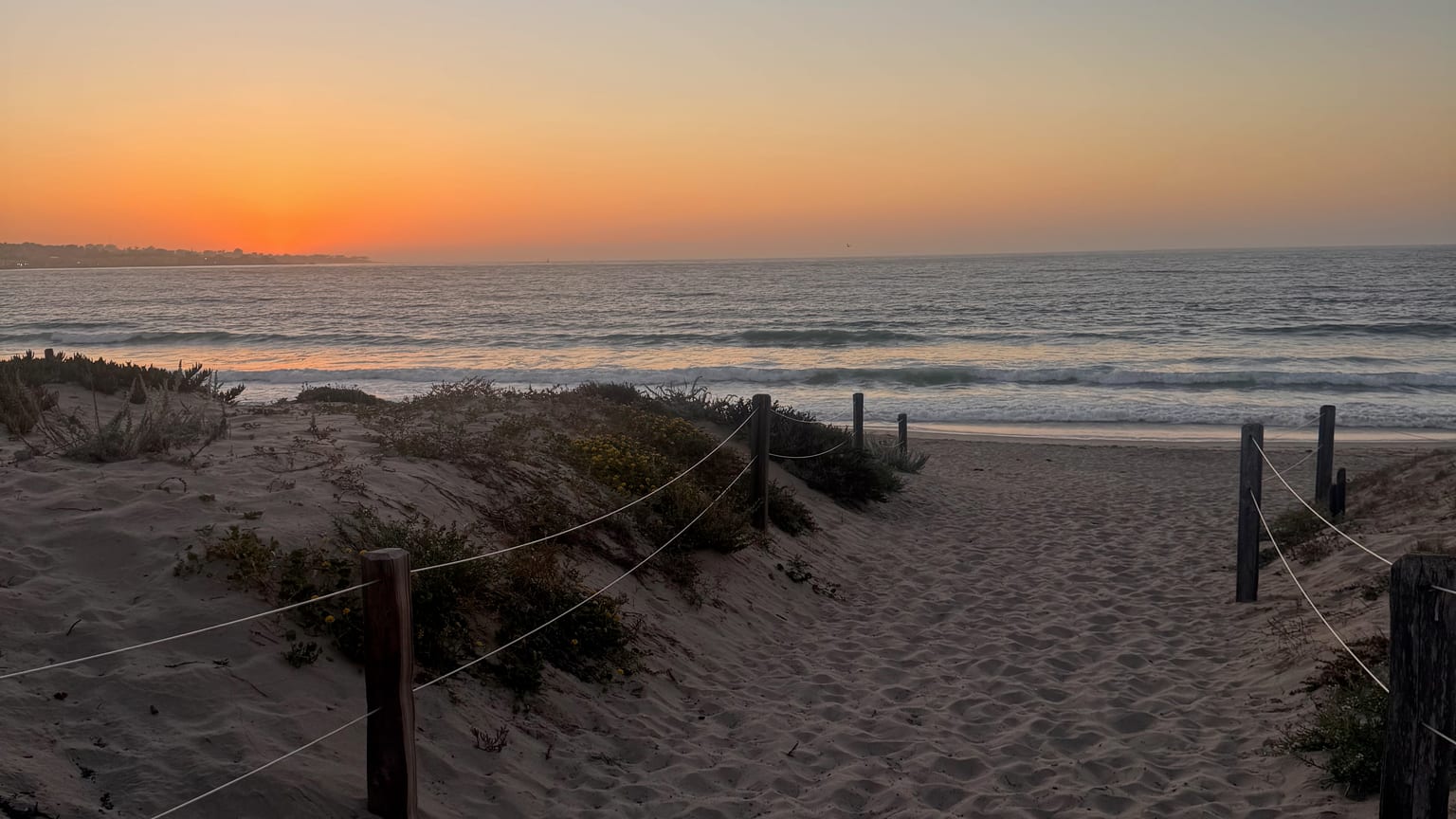 Sunset over Del Monte Beach in Monterey, California with sandy dune path leading to the waves
